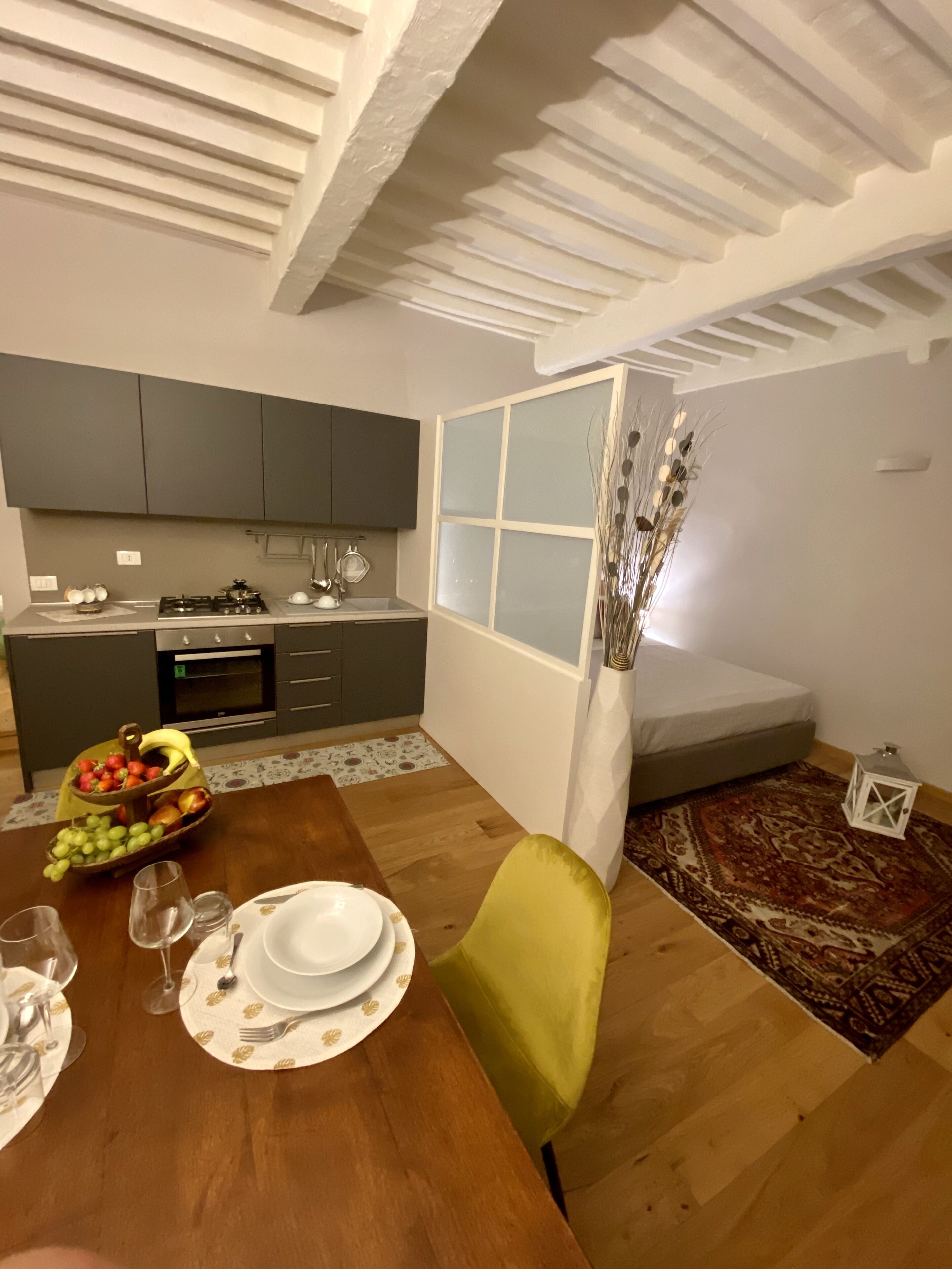 A modern kitchen with grey cabinets, a dining table set with plates and glasses, and a decorative vase with dried plants.