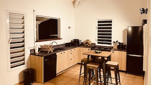 A modern kitchen with wooden cabinets, a black refrigerator, and a dining area with stools. - Villa Samathan 3 bedrooms private pool 5mn from the beach (Saint-François)