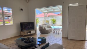 A living room with a TV, sofa, coffee table, and a view of a pool and outdoor furniture. - Villa Samathan 3 bedrooms private pool 5mn from the beach (Saint-François)