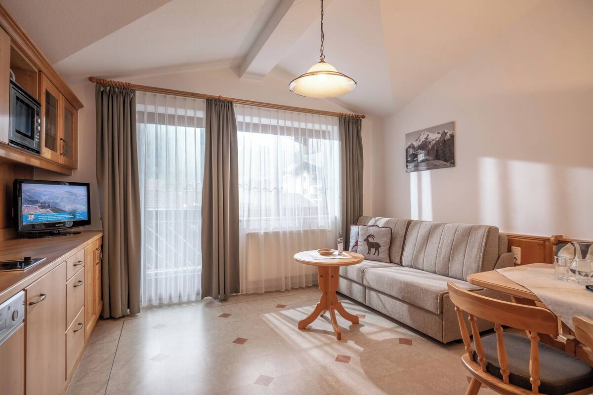 Una sala de estar moderna con un sofá, una mesa de comedor, un televisor y una zona de cocina con armarios y un microondas.