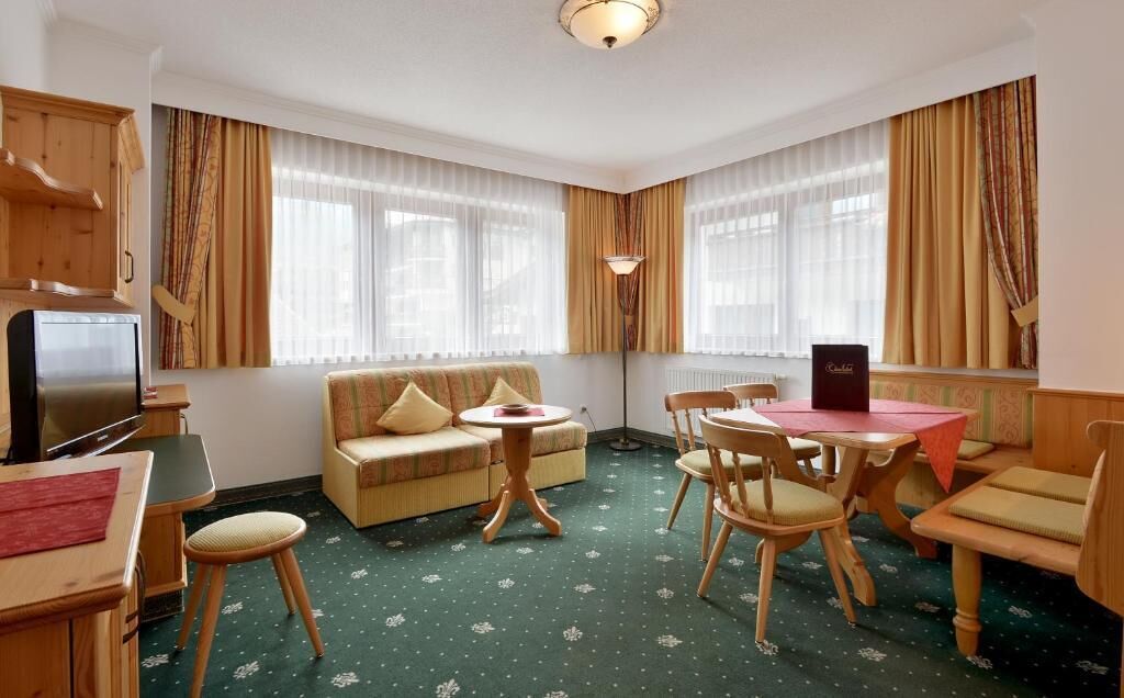 A room with a sofa, dining table, chairs, a television, and a radiator.