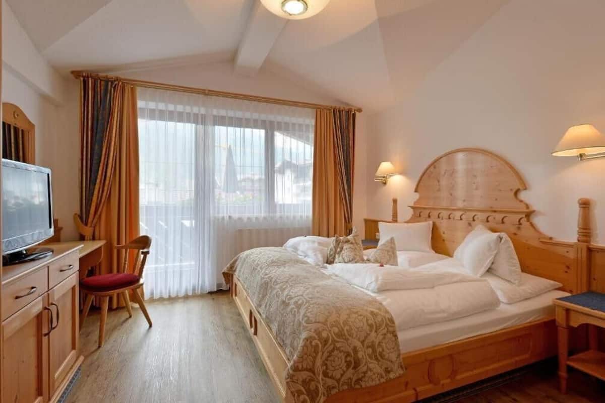 Una habitación de hotel con una cama de madera, televisor, escritorio y una silla.