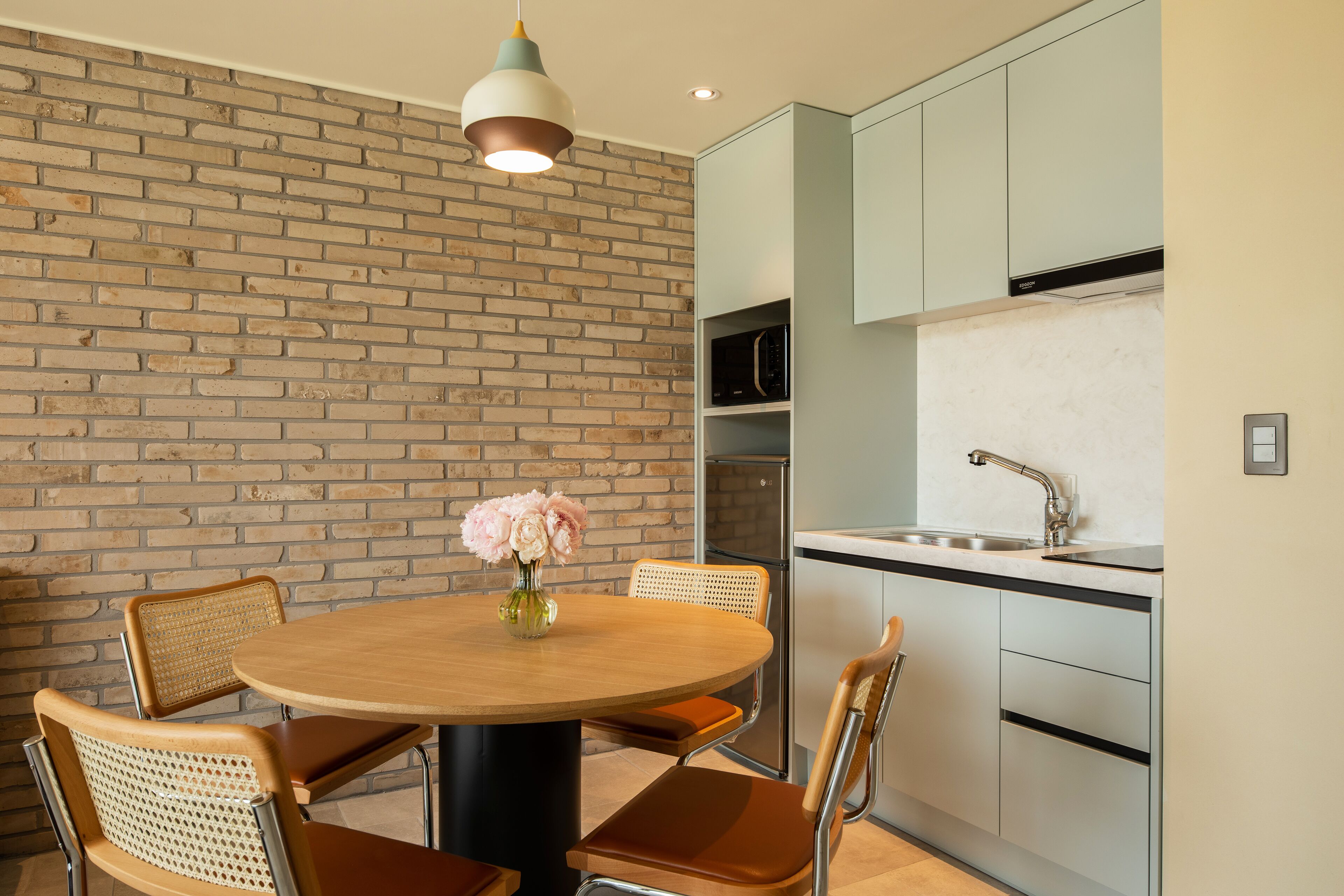 A modern kitchen with a brick wall, a round wooden table, and four chairs.