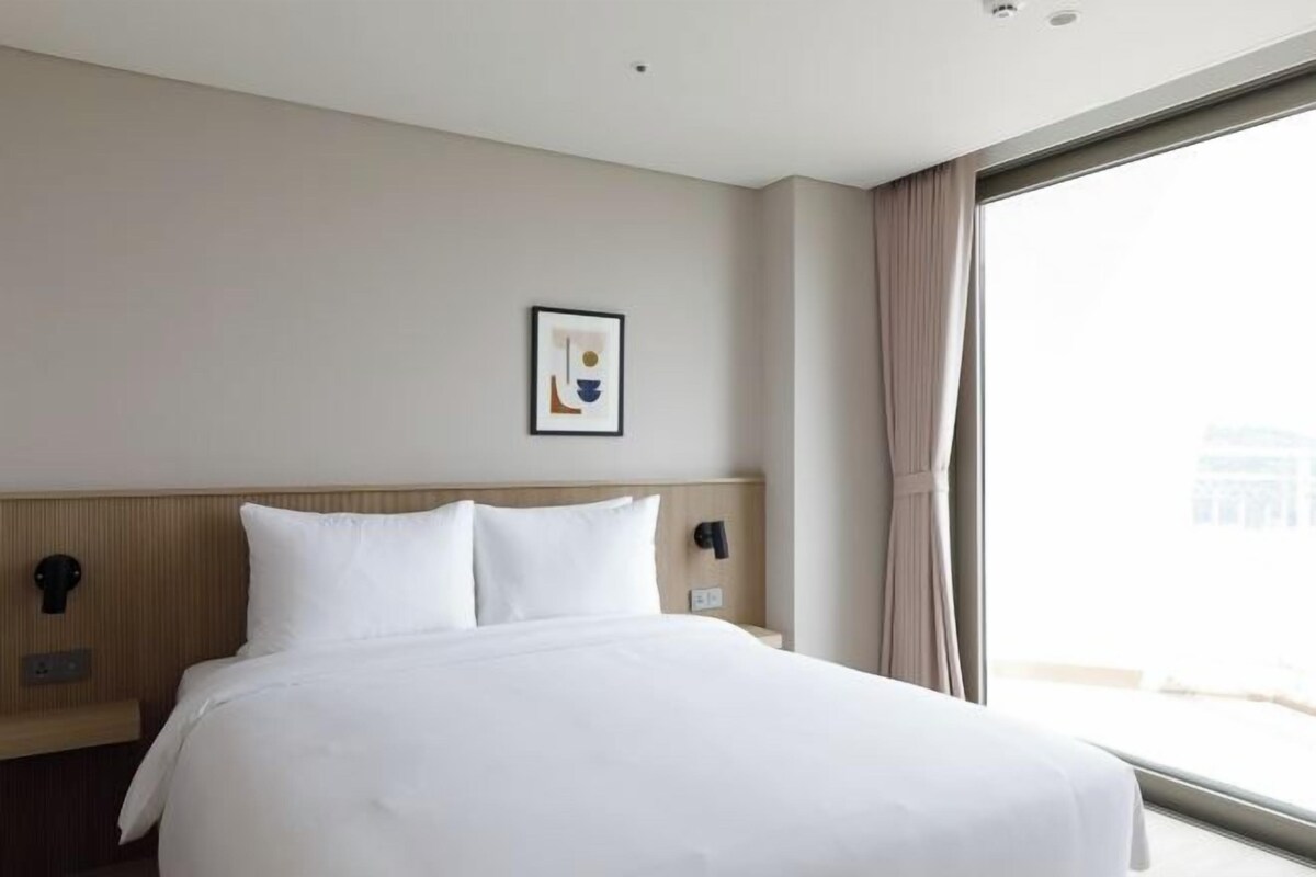 Habitación de hotel con una cama grande, una mesita de noche, una lámpara de pared y un ventanal con cortinas.