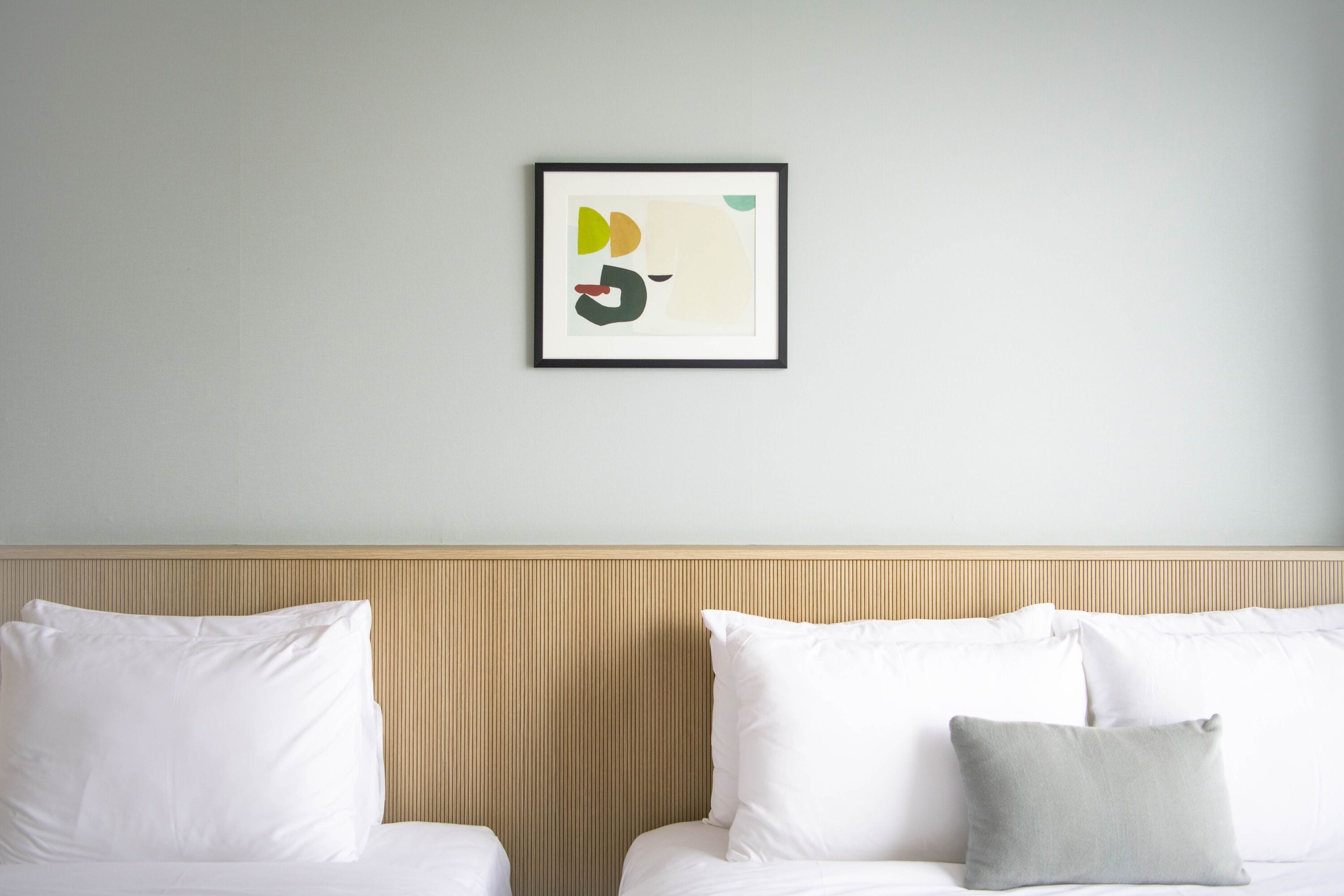 A hotel room with two beds, a headboard, and a framed abstract art piece on the wall.