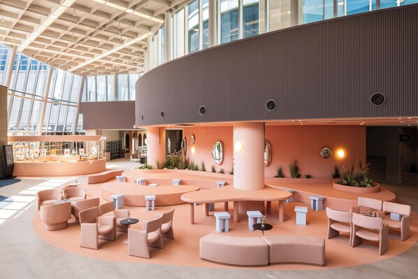 A spacious indoor area with multiple seating arrangements, including sofas and tables, and a large open space with a high ceiling and large windows.