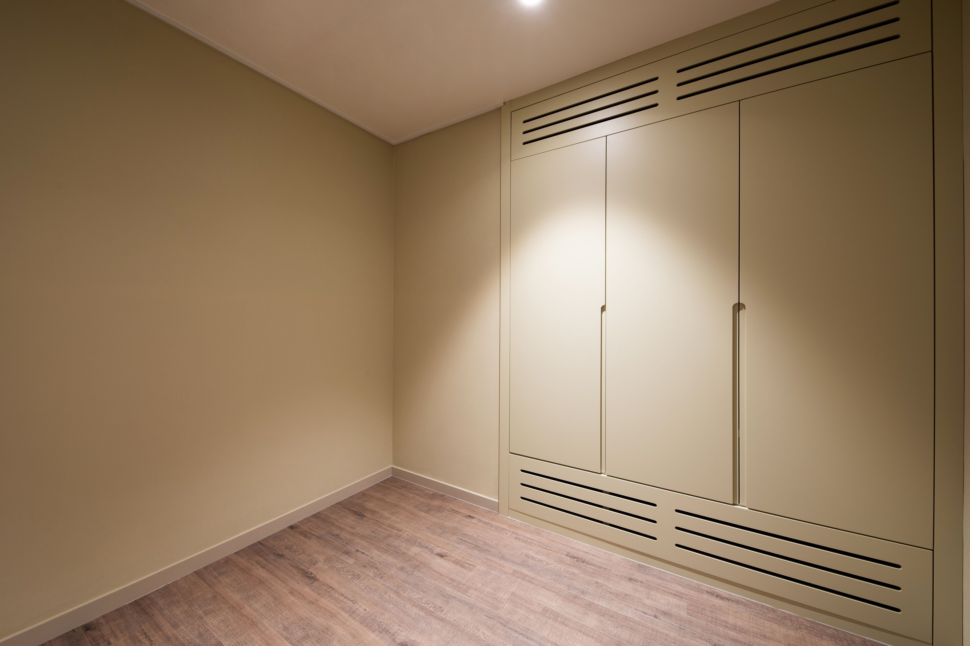 Et værelse med beige vægge, trægulv og en stor garderobe med ventilationsåbninger.