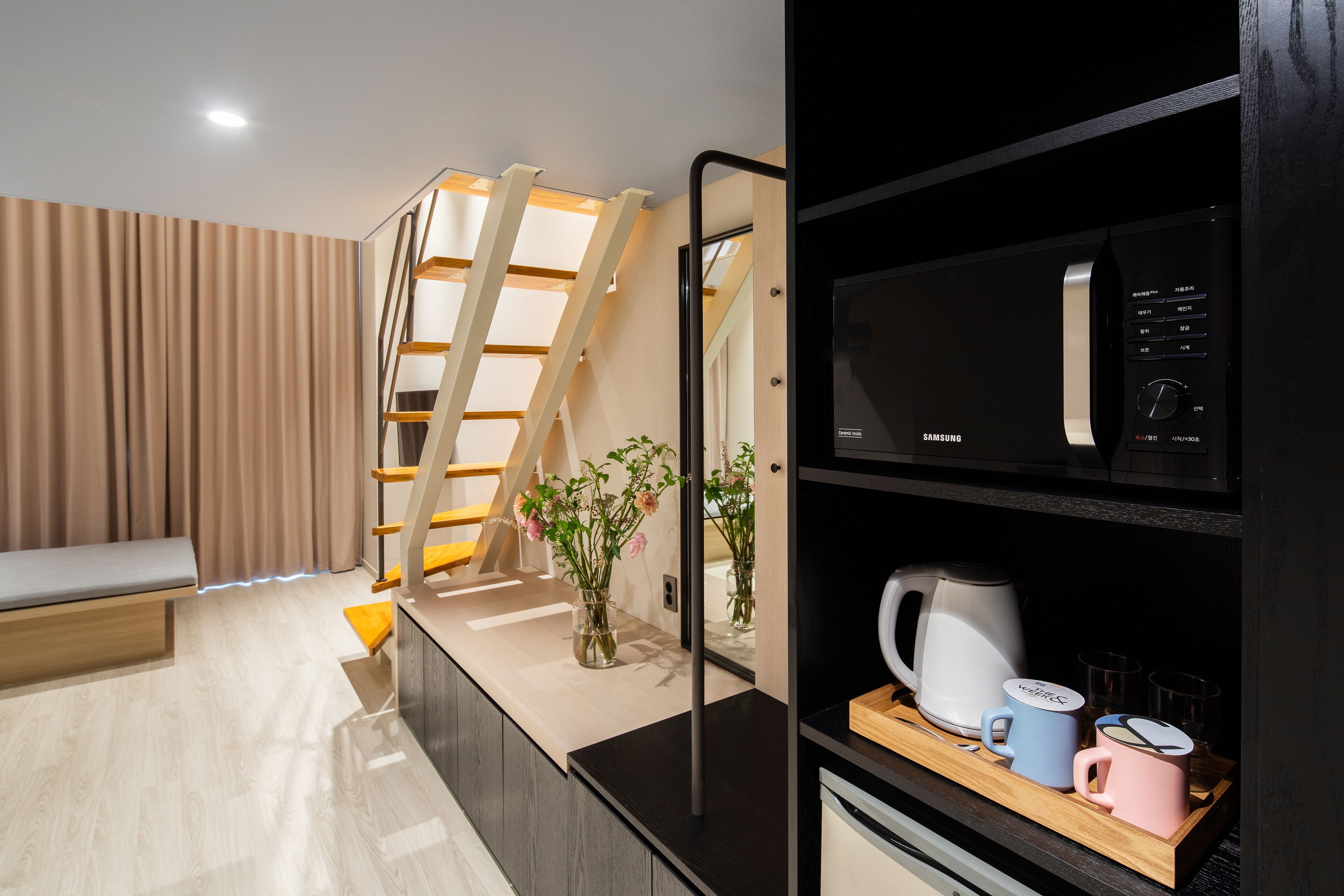 A modern kitchen with a microwave, kettle, and mugs on the counter.