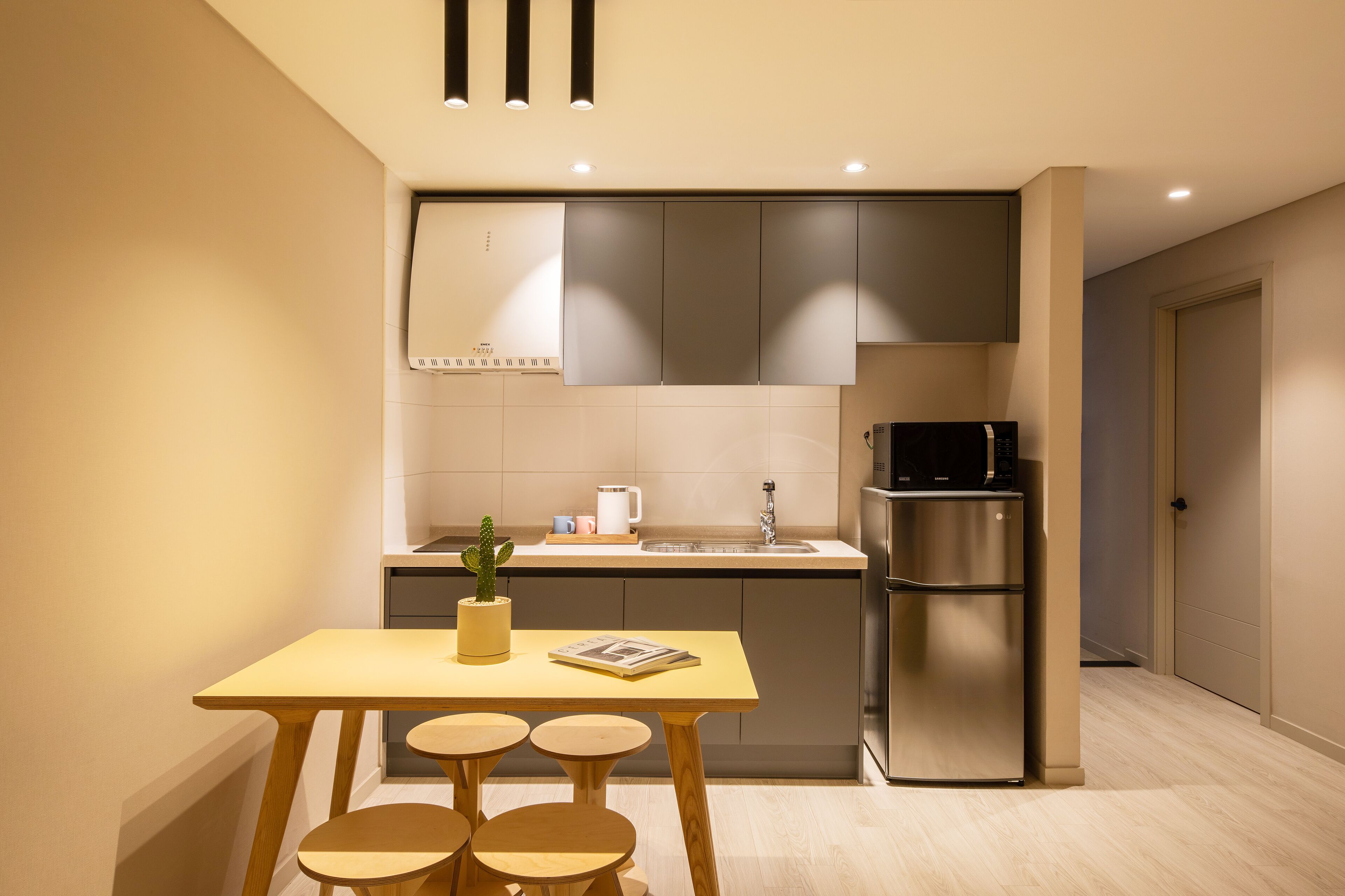 A modern kitchen with a wooden table and stools, a refrigerator, and a sink.