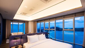 Habitación de hotel moderna con una cama grande, una mesita de noche, una lámpara y vista al mar.