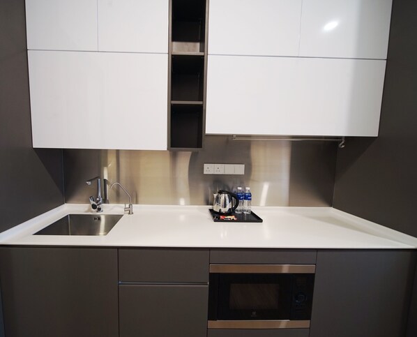 A modern kitchen with a stainless steel sink, a built-in oven, and a microwave. There are two bottles of water and a kettle on the counter. - Ceylonz Suites by MyKey (Kuala Lumpur)