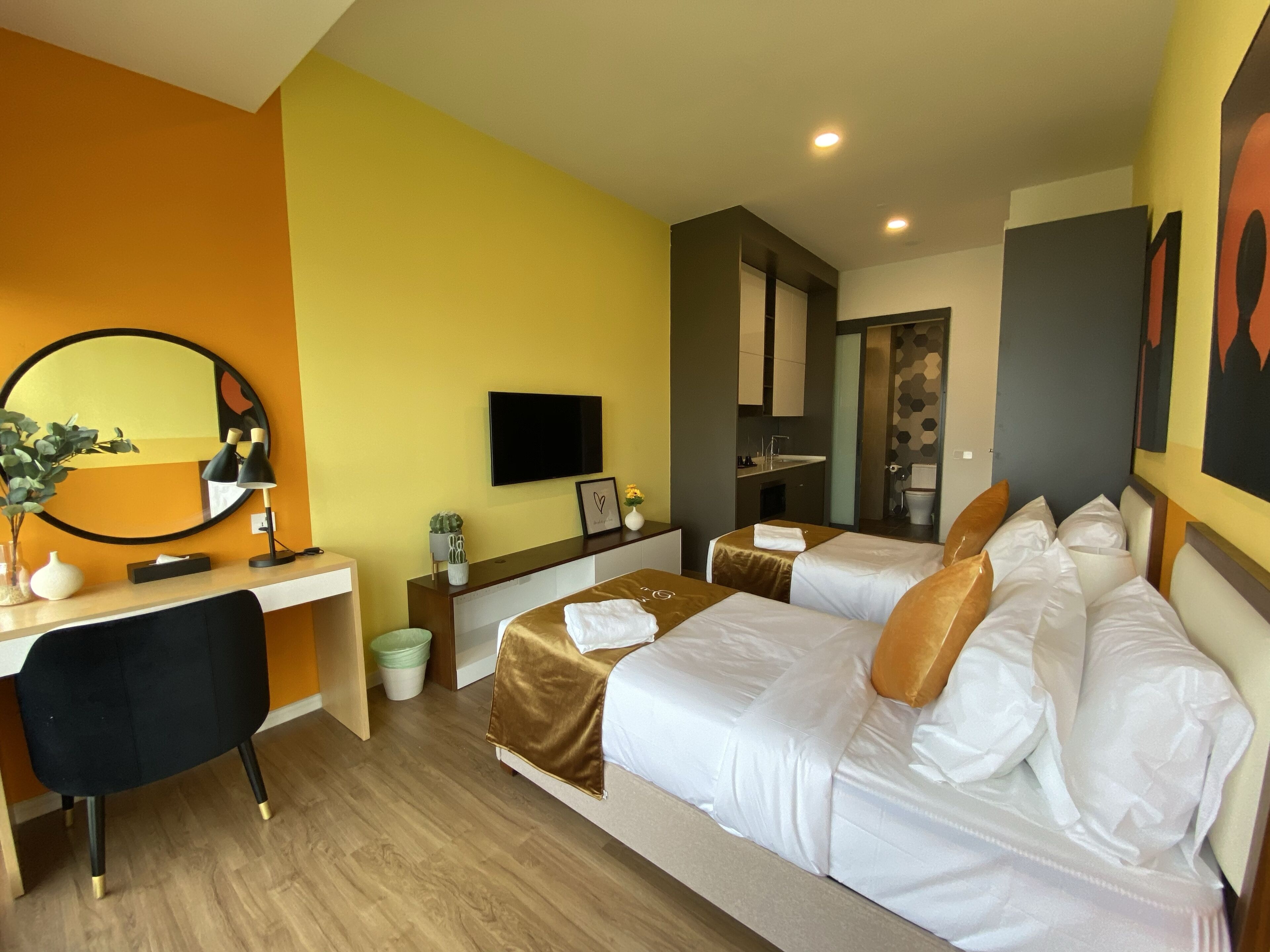 Hotelkamer met twee bedden, een bureau, een spiegel, een televisie en een zichtbare badkamer door een open deur.