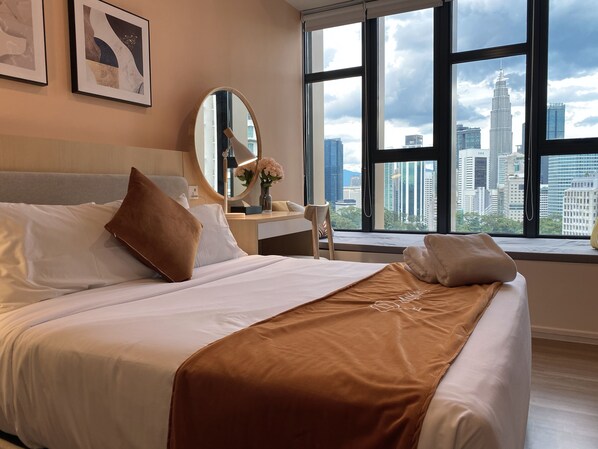 A hotel room with a large bed, a desk, a mirror, and a window with a city view.