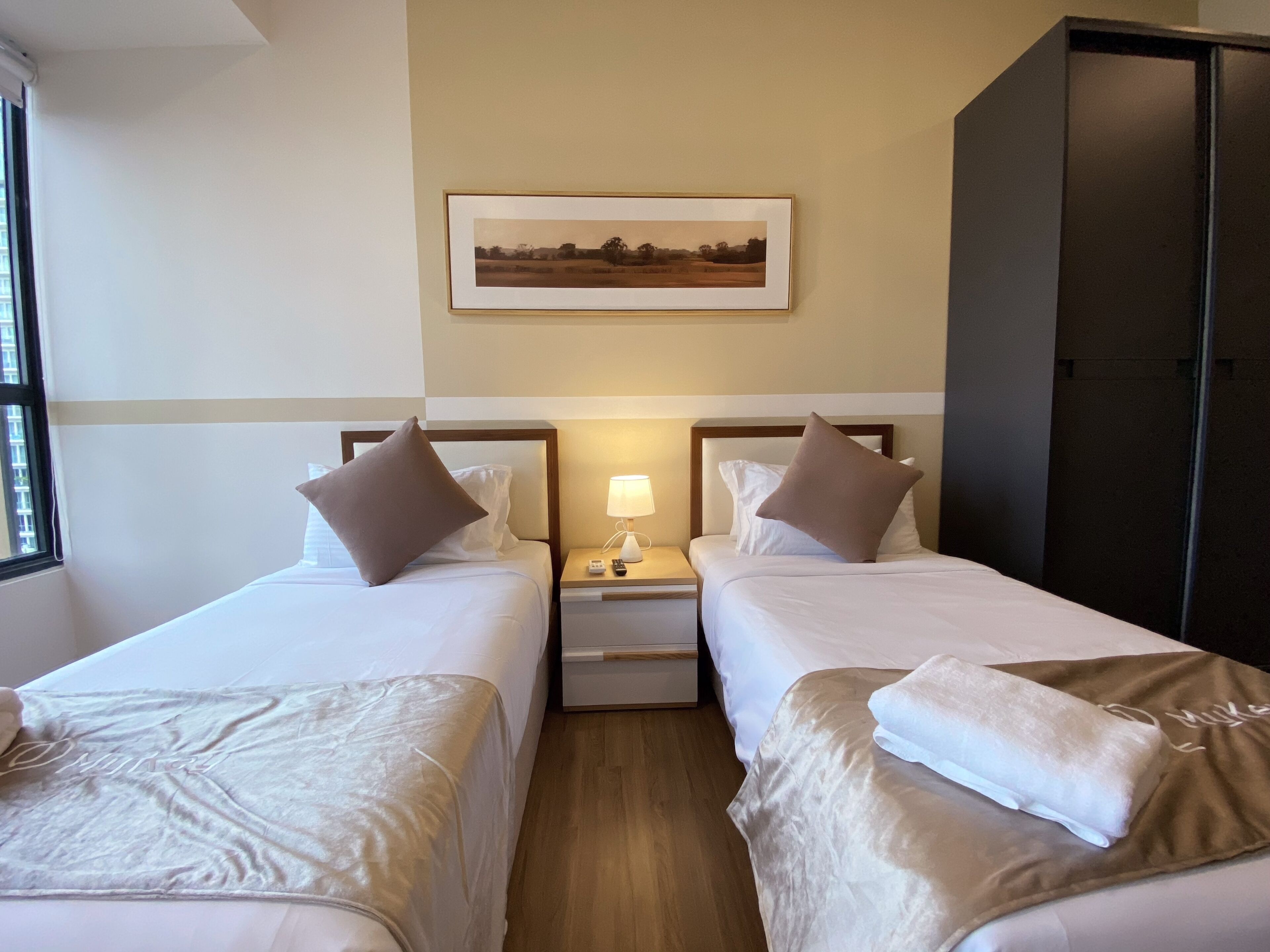 Habitació d'hotel amb dos llits, una tauleta de nit amb una làmpada, un quadre amb marc a la paret i un armari.