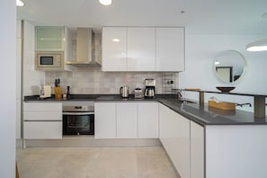 Een moderne keuken met witte kastjes, een magnetron, een koffiezetapparaat en een spoelbak.