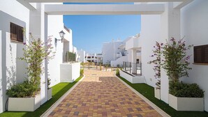 A pathway leading to a row of white buildings with balconies, surrounded by planters with flowering plants. - Apartamento Marion (Mar de Pulpi) (Almería)