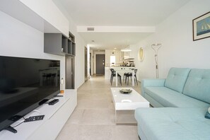 Un salon moderne avec un téléviseur à écran plat, un canapé, une table basse et un coin repas à l’arrière-plan.
