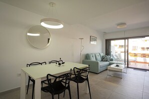 Un salon moderne comprenant une table à manger, des chaises, un canapé et une table basse. Un grand miroir est accroché au mur, ainsi qu’un cadre avec une image.