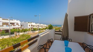 A balcony with a table and chairs, overlooking a coastal area with white buildings and a clear sky.