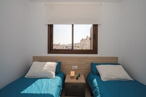 Ein Schlafzimmer mit zwei Betten, einem Fenster mit Blick auf Gebäude und einem Nachttisch mit einer Lampe und zwei Vasen.