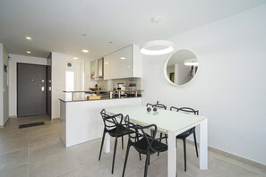 A modern kitchen with white cabinets, a dining table with four chairs, and a large mirror on the wall.