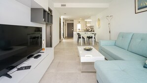 A modern living room with a flat-screen TV, a sofa, a coffee table, and a dining area in the background.