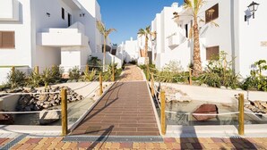 A pathway leading through a white building complex with palm trees and a small water feature.