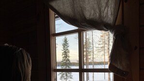Una persona sentada junto a una ventana con vista a un paisaje nevado y una vela sobre la mesa.