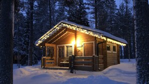Una cabaña de madera con porche, rodeada de árboles cubiertos de nieve.