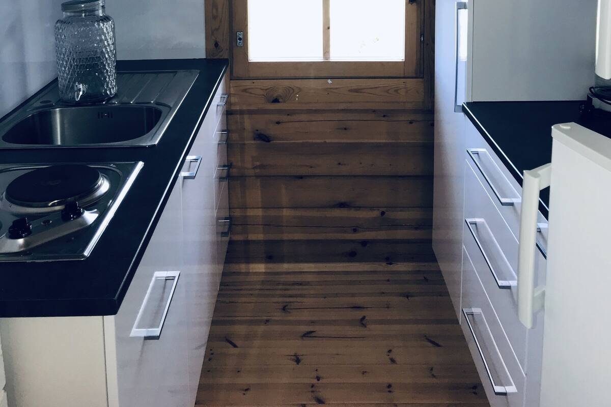 Une cuisine de taille réduite avec des murs en bois, une fenêtre avec un rideau et les équipements de base.
