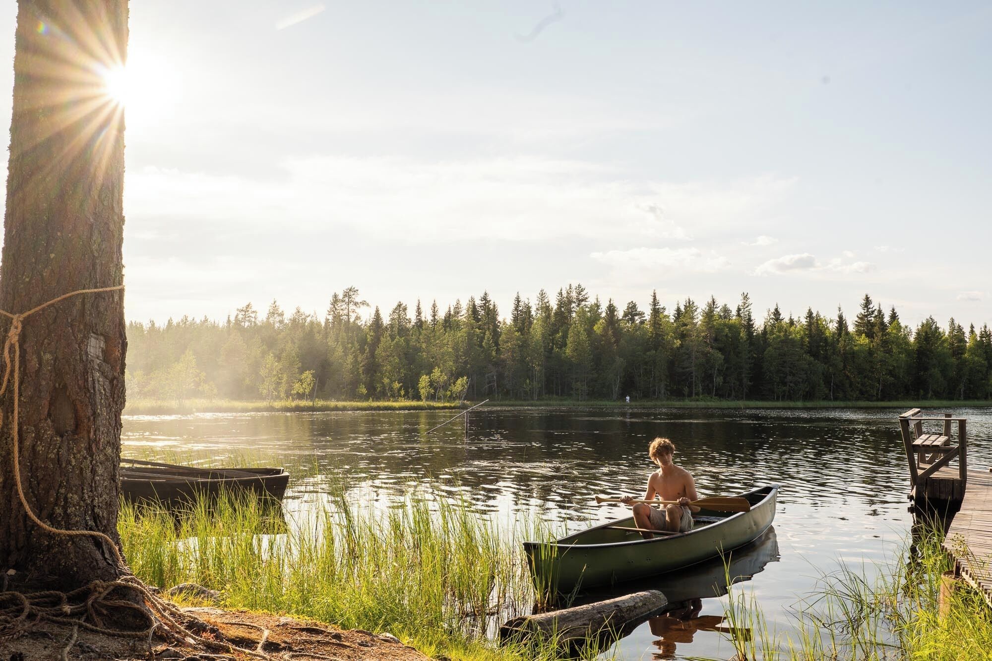 Una tranquilla scena di un lago con un pontile, una barca e una persona in un canoa.