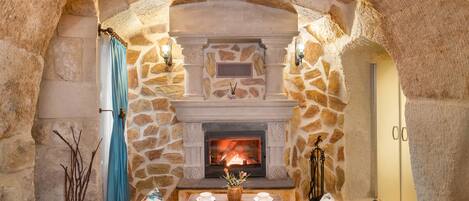 A stone-walled room with a fireplace, a sofa, and a table with a vase.