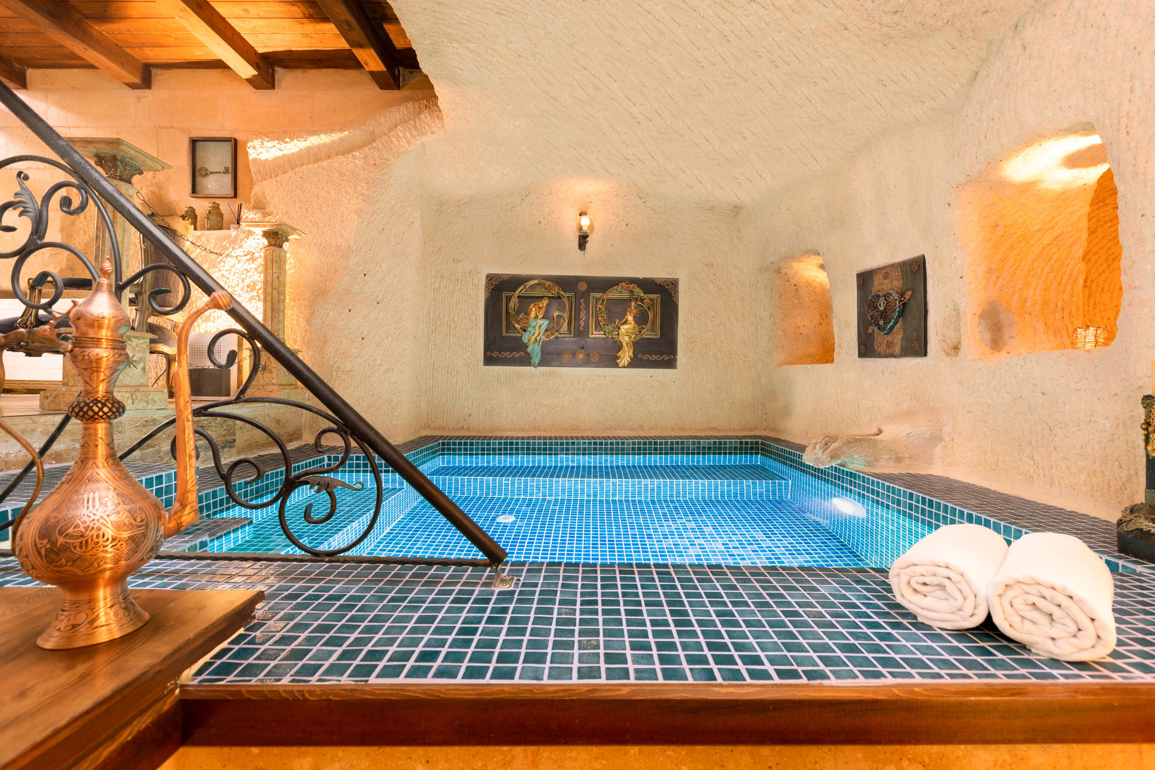 A traditional Turkish bath with a blue-tiled floor, a wooden bench, and a copper vessel.