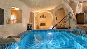 Una habitación de paredes de piedra con una piscina de azulejos azules, una chimenea y una escalera.