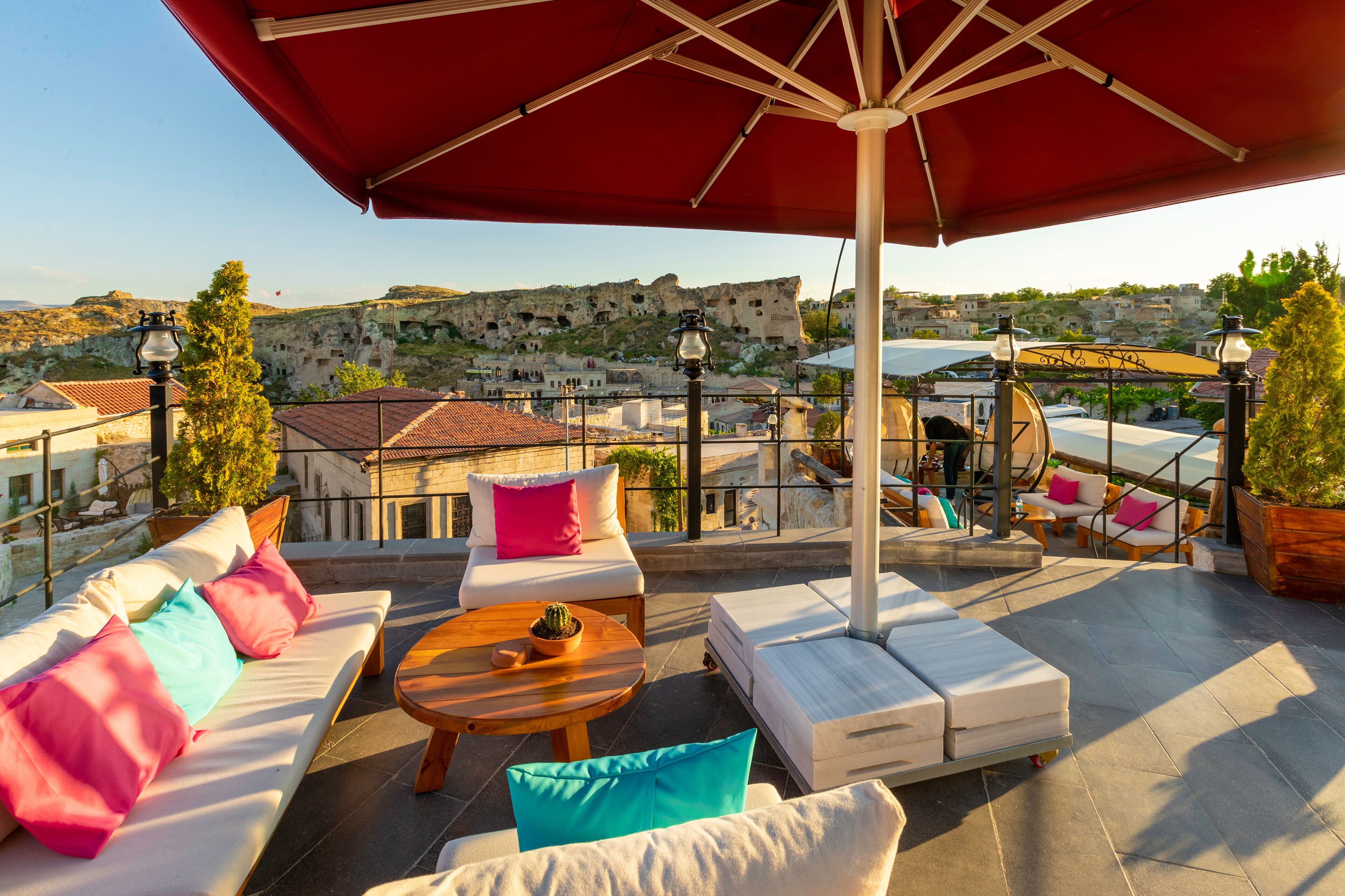 Terraza en la azotea con mobiliario exterior, vistas a edificios históricos y una sombrilla roja que da sombra.