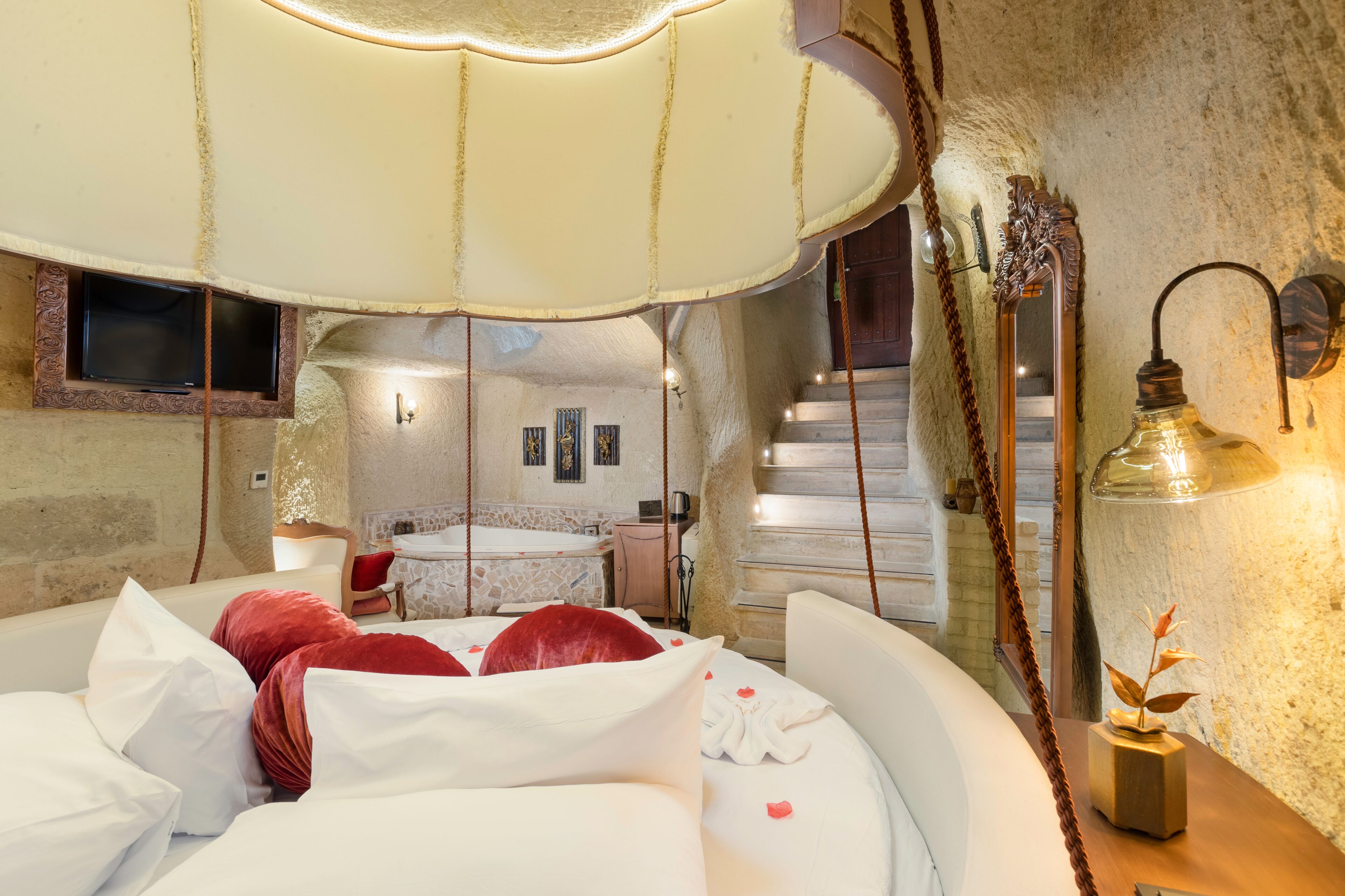 Un dormitorio con una cama grande, una lámpara colgante, un espejo y vistas a un baño y una escalera.