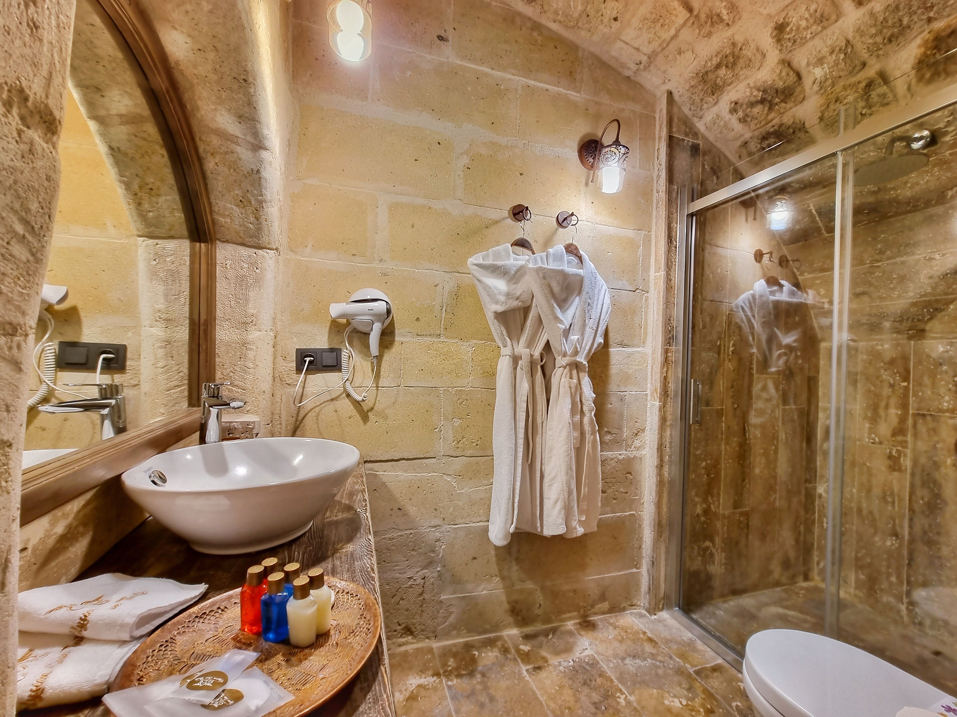 A bathroom with a large mirror, a sink, a glass shower enclosure, and a towel rack with robes.