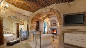 Un interior rústico de piedra con chimenea, un sofá, un televisor montado en la pared y un banco de piedra.