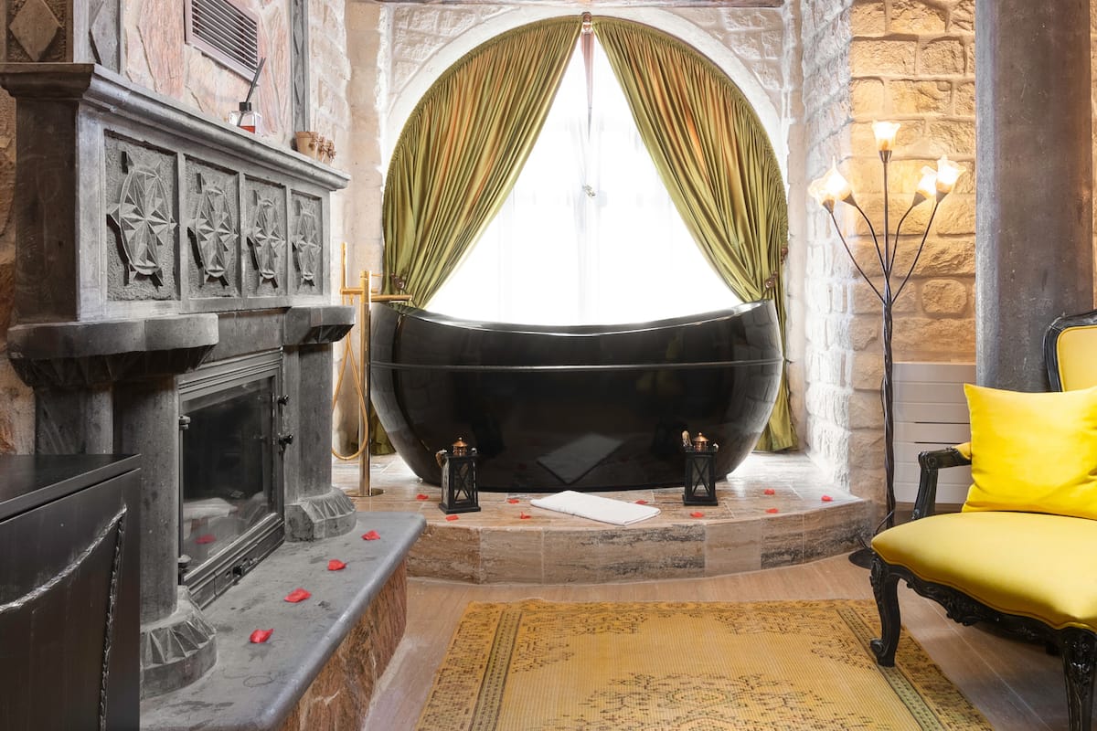 A room with a large bathtub, a fireplace, and a yellow chair.