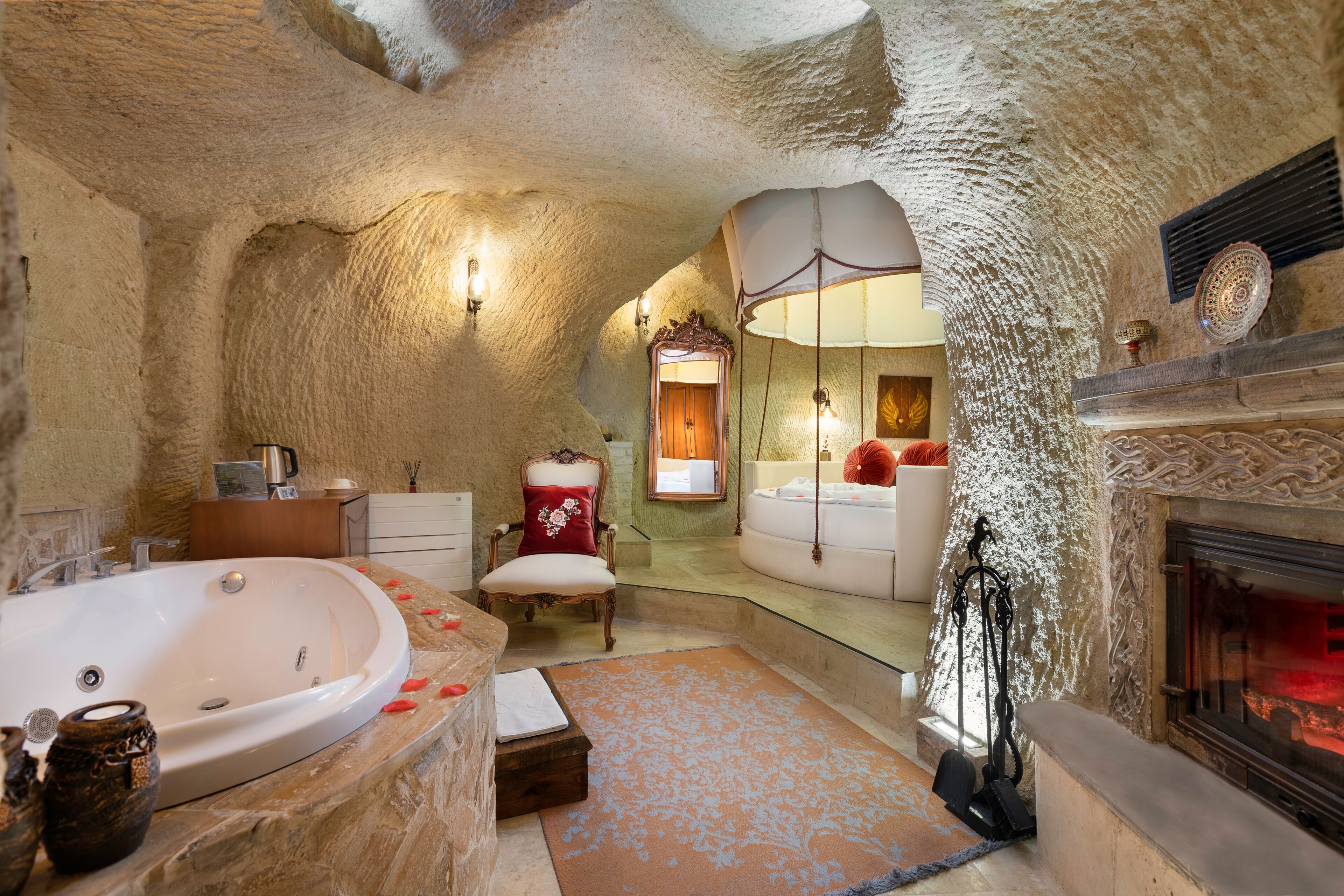 A bathroom with a large bathtub, a mirror, a chair, and a fireplace.