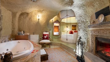 A bathroom with a large bathtub, a mirror, a chair, and a fireplace.