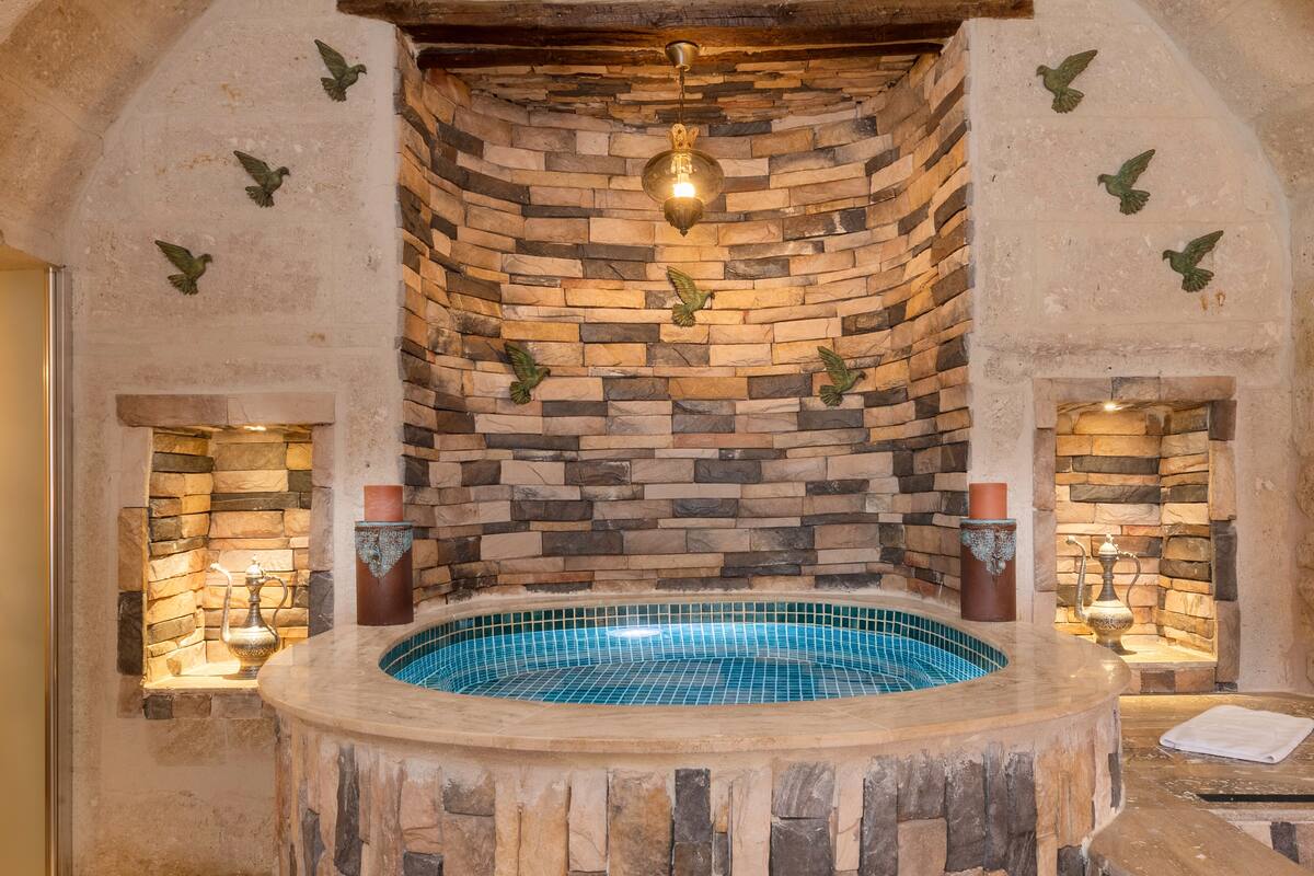 A stone-walled hot tub with a tiled interior, surrounded by stone walls and decorative elements.