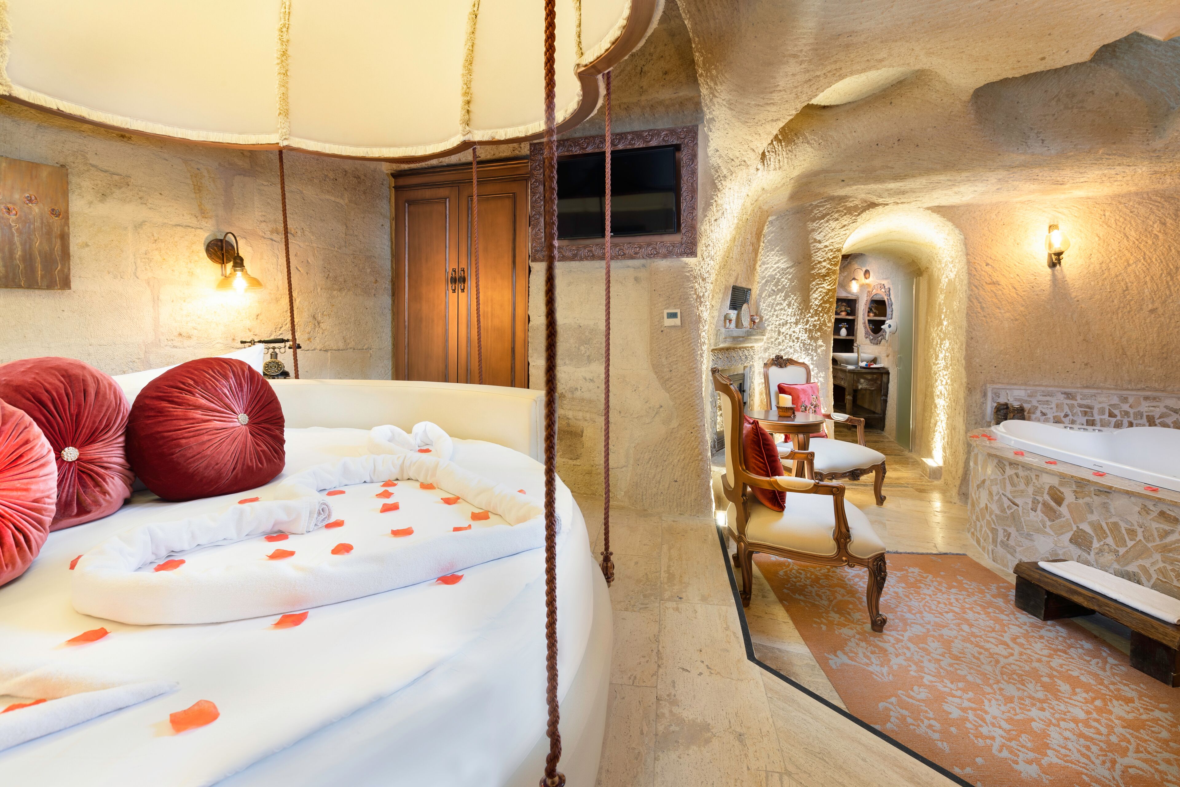 A luxurious bedroom with a large bed, a stone wall, a wooden cabinet, and a small table with chairs.