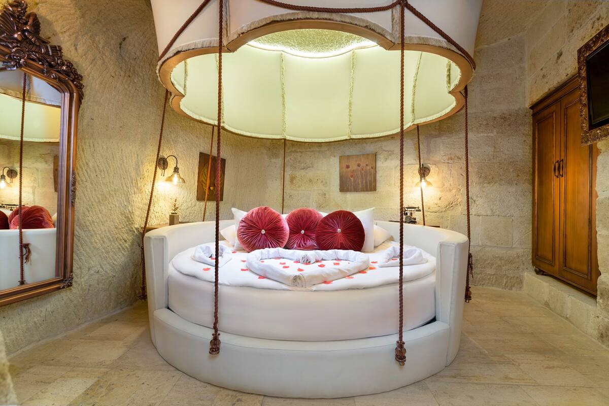 A circular bed with a canopy, a stone wall, and a wooden cabinet.