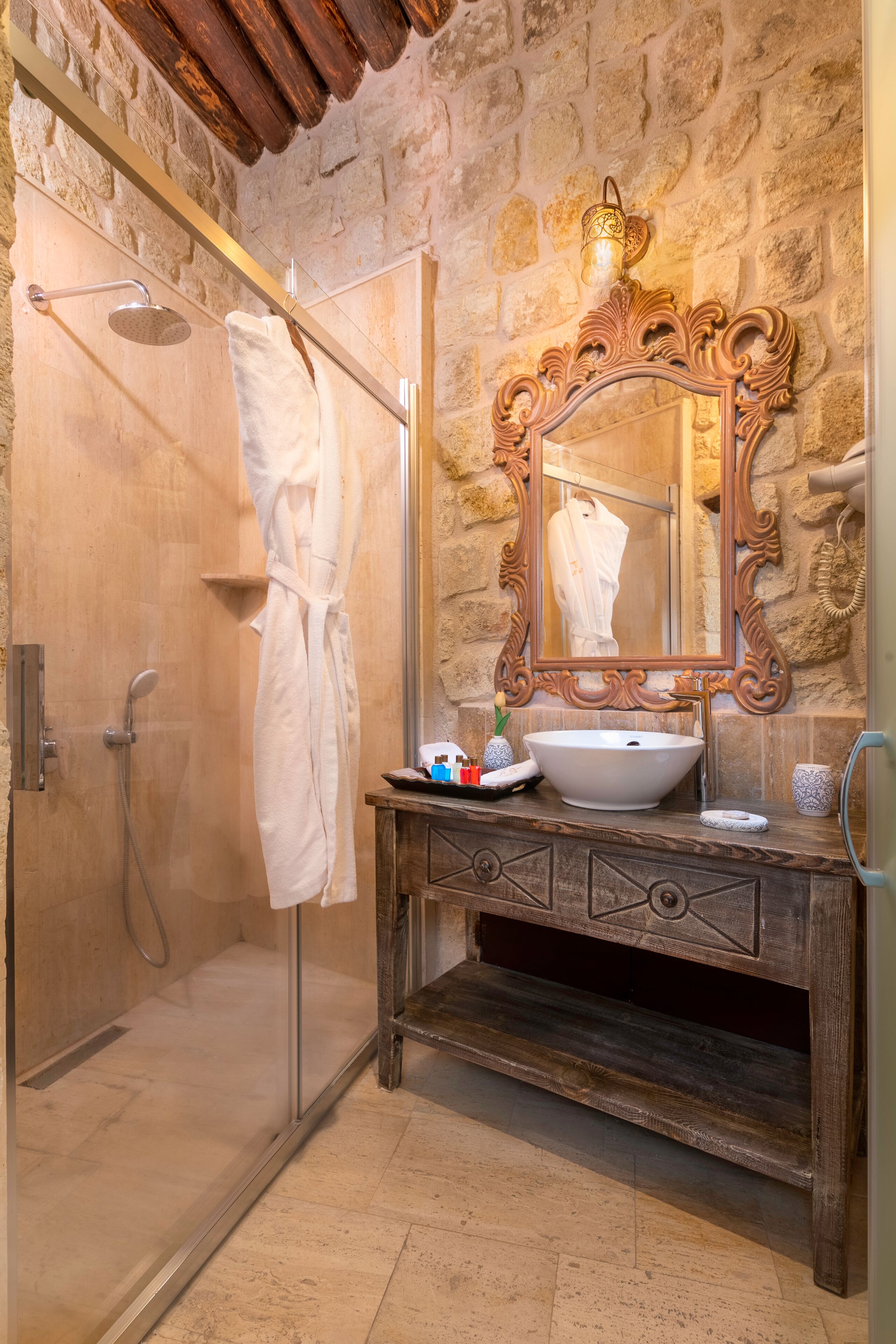 A bathroom with a stone wall, a wooden vanity, a large mirror, and a glass shower enclosure.