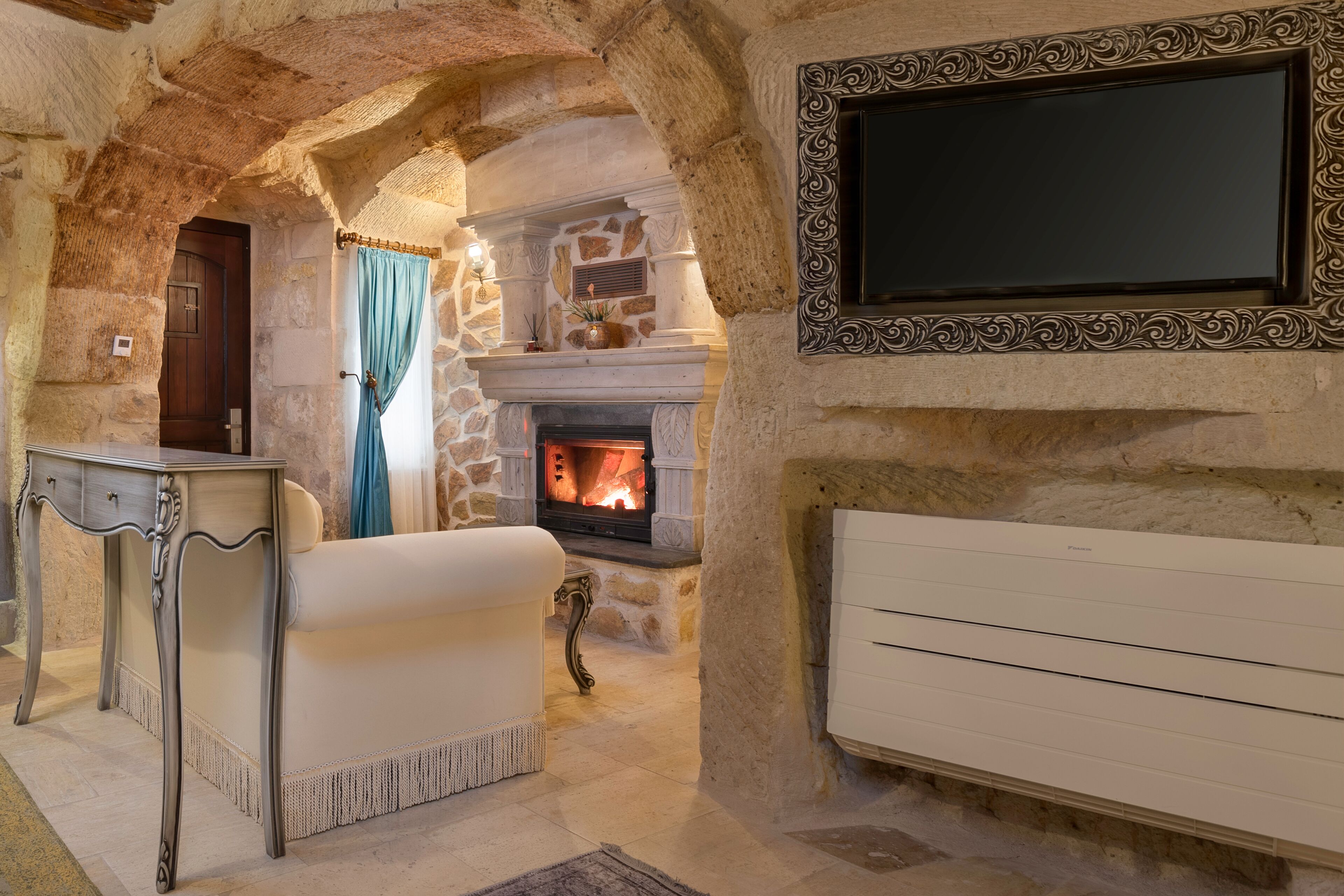 Ein Zimmer mit Steinwänden, einem Kamin, einem weißen Sofa und einem an der Wand befestigten Fernseher.