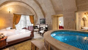 Habitación de hotel con una cama grande, un área de descanso con sillas, un televisor y una bañera de hidromasaje.