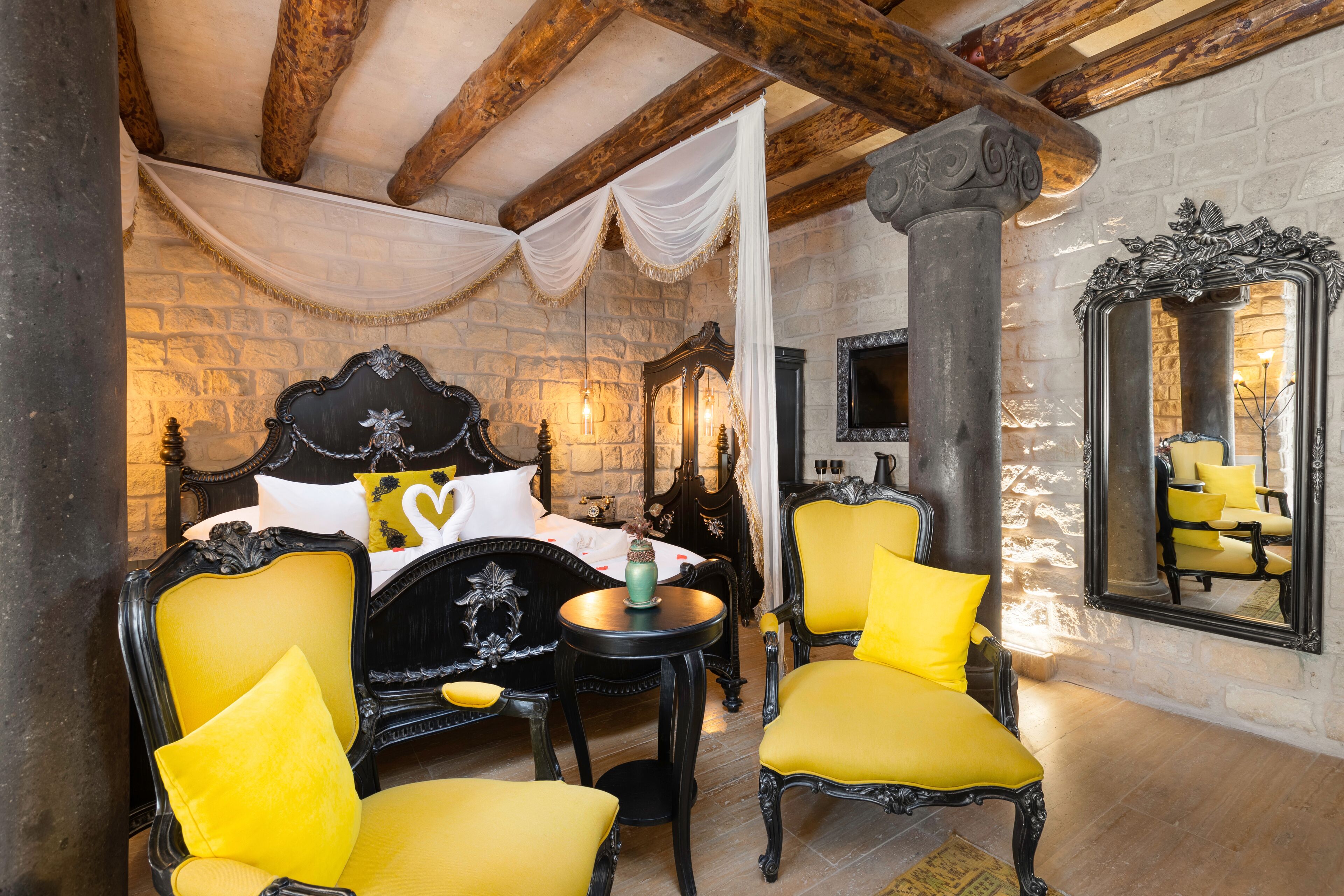 Una habitación con una cama, dos sillas, una mesa, un espejo y una pared de piedra.