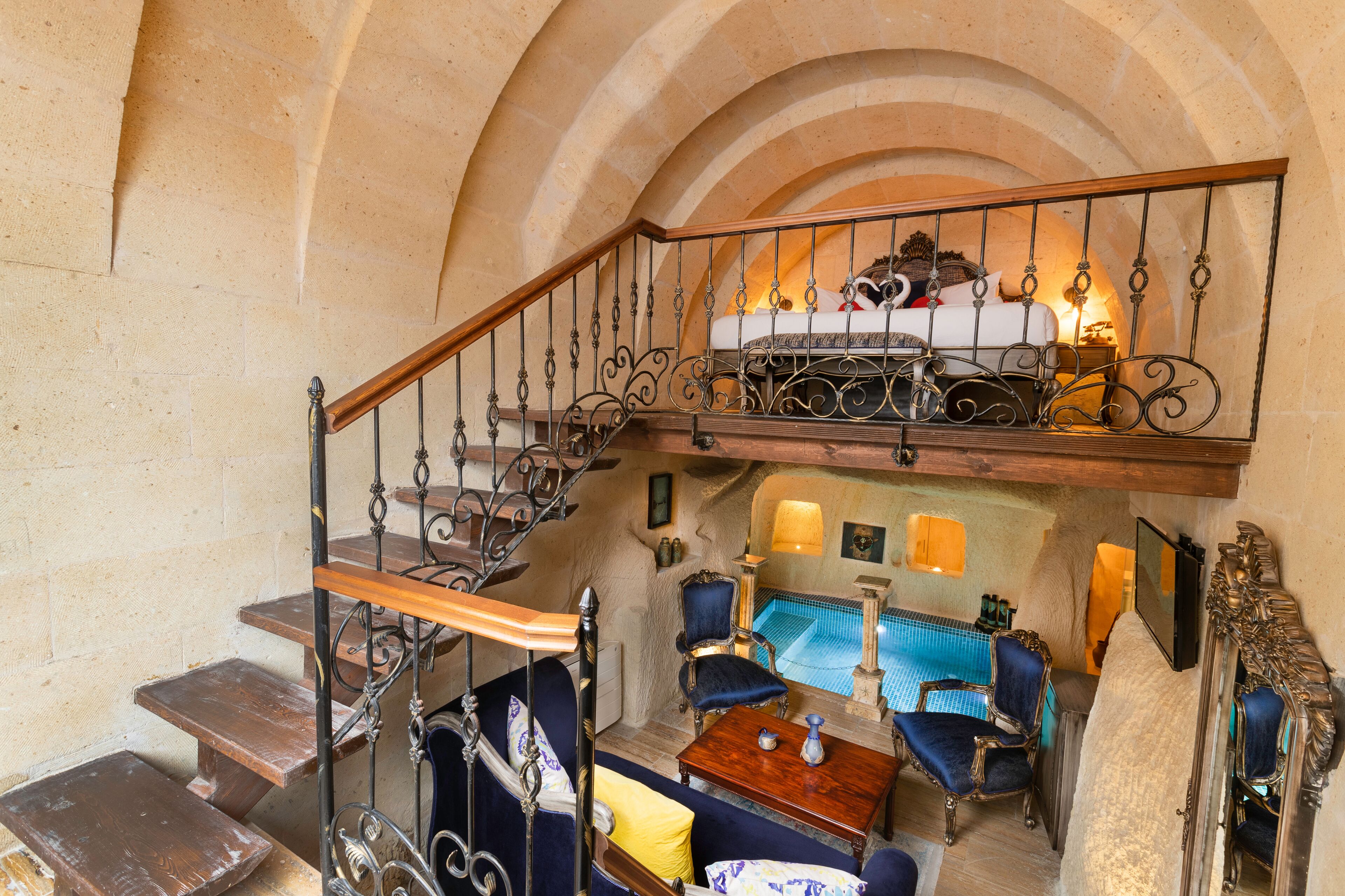 A room with a wooden staircase, a bed with a canopy, a blue armchair, a small table, and a mirror.