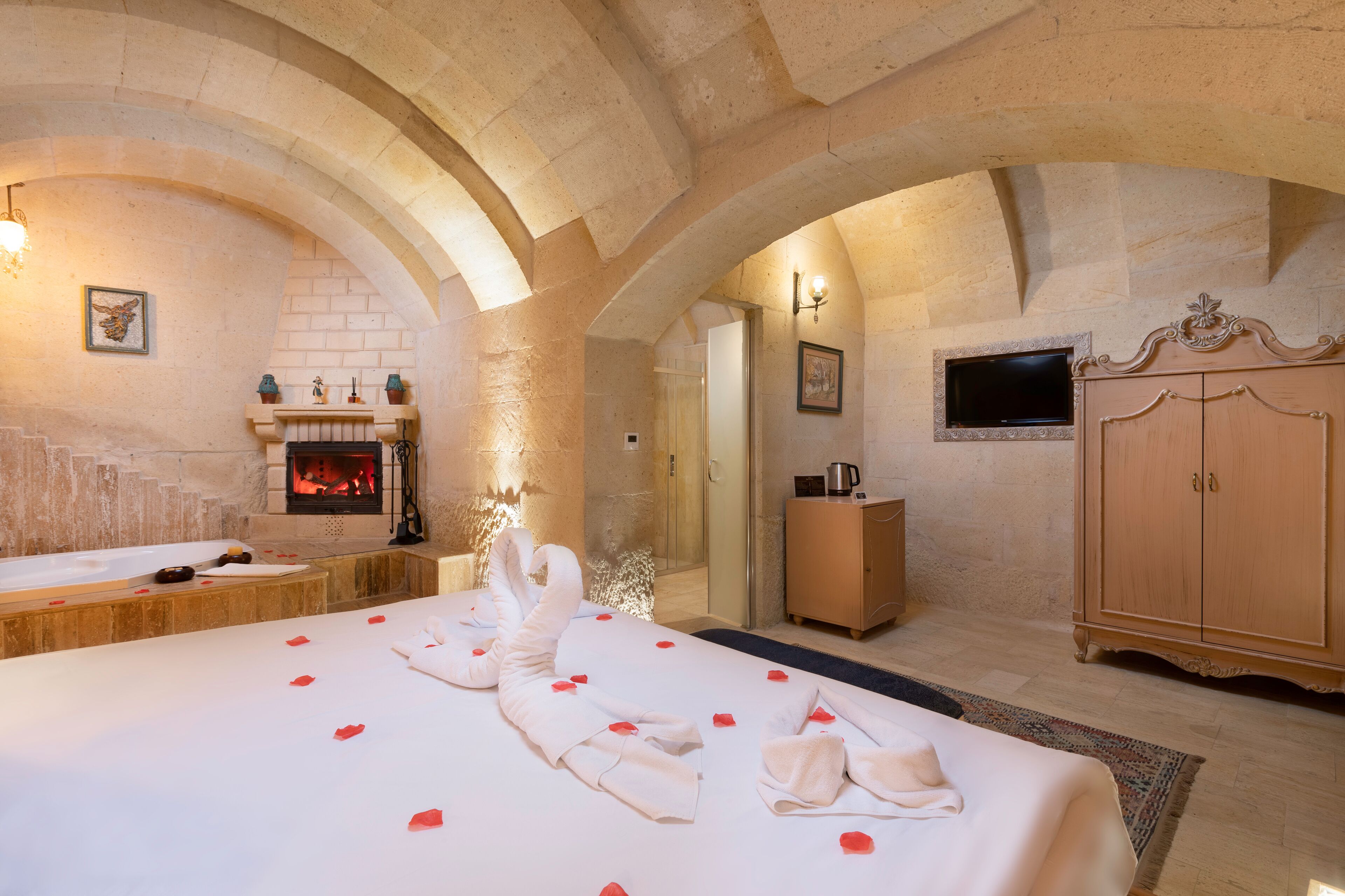 A room with a large bed, a fireplace, a television, and a wooden cabinet.